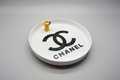 White tray with Chanel logo and yellow coffee pot on a gray surface