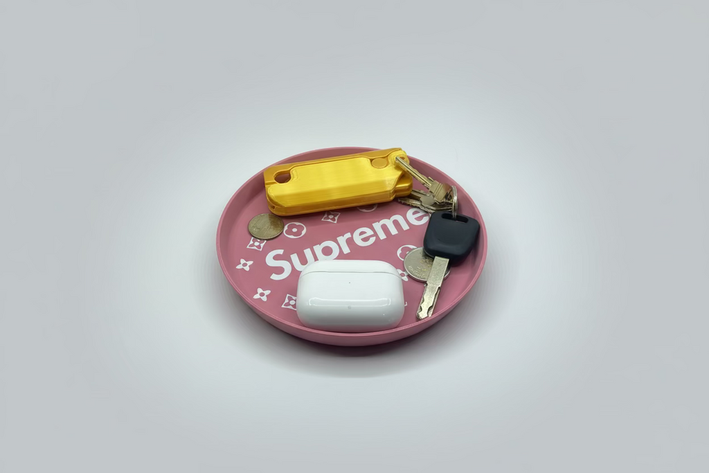 Pink Supreme plate with a yellow keychain, white case, and keys on a gray surface.