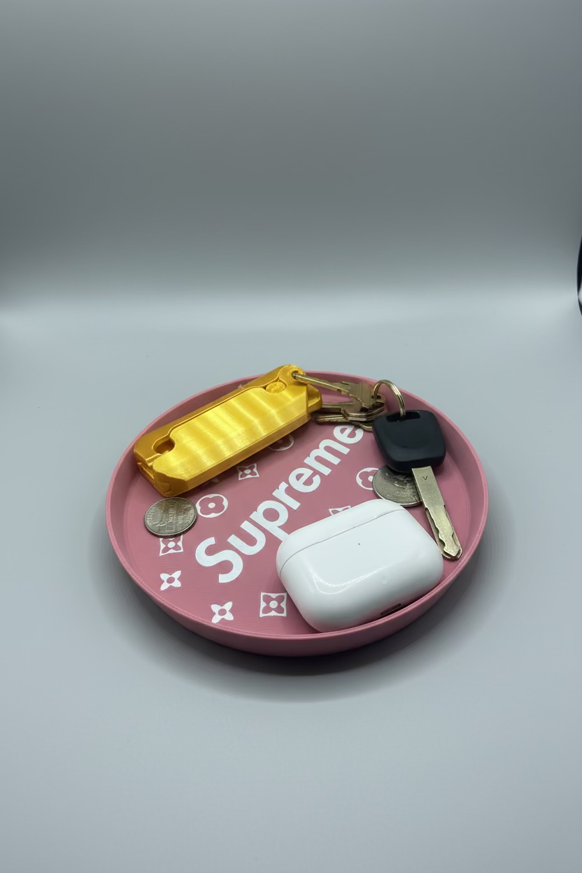 Pink 'Supreme' tray with keys, airpod case, and coins on a gray surface.