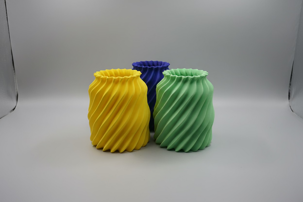 Three colorful 3D-printed vases on a printing bed.