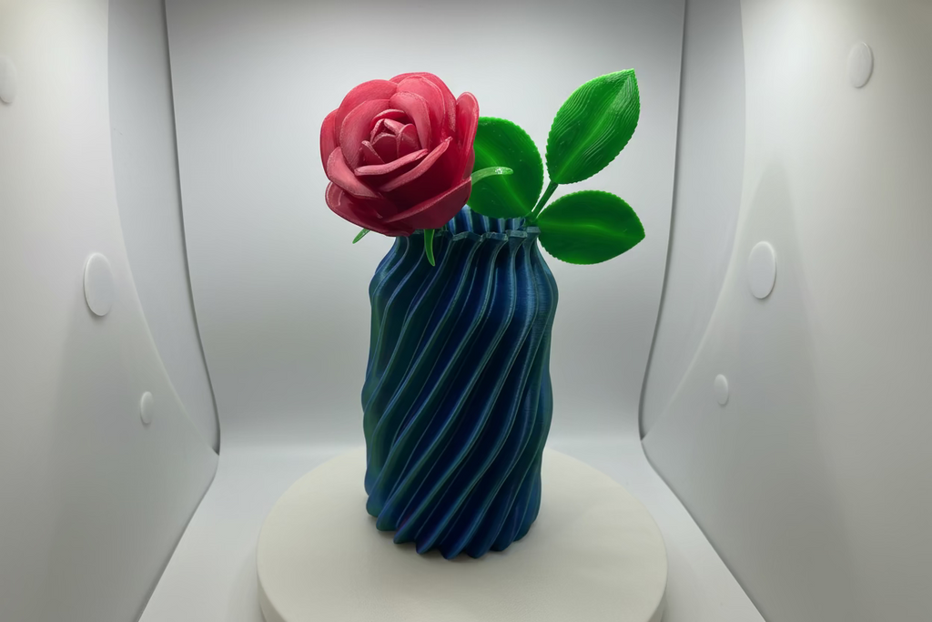 3D-printed vase with a red flower and green leaves on a white surface