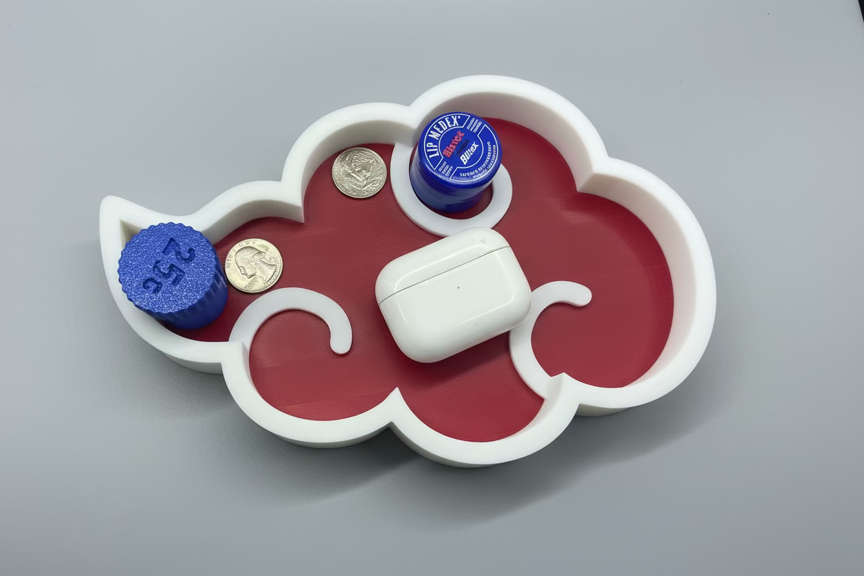 Cloud-shaped tray with a white air pod, blue bottle cap, and gold coins on a gray surface.